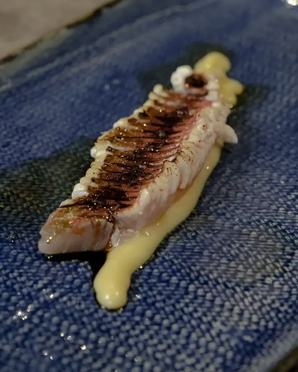 Peix amb la superfície marcada, servit amb salsa en un plat blau